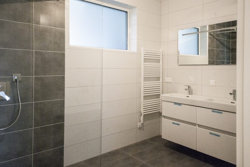 Bad mit dunkler Fliesenwand, Dusche und Doppelwaschtisch
