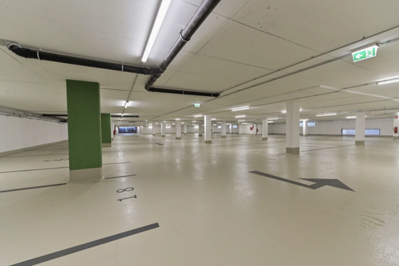 Tiefgarage mit grünen Stützen, markierten Stellplätzen und Richtungspfeil
