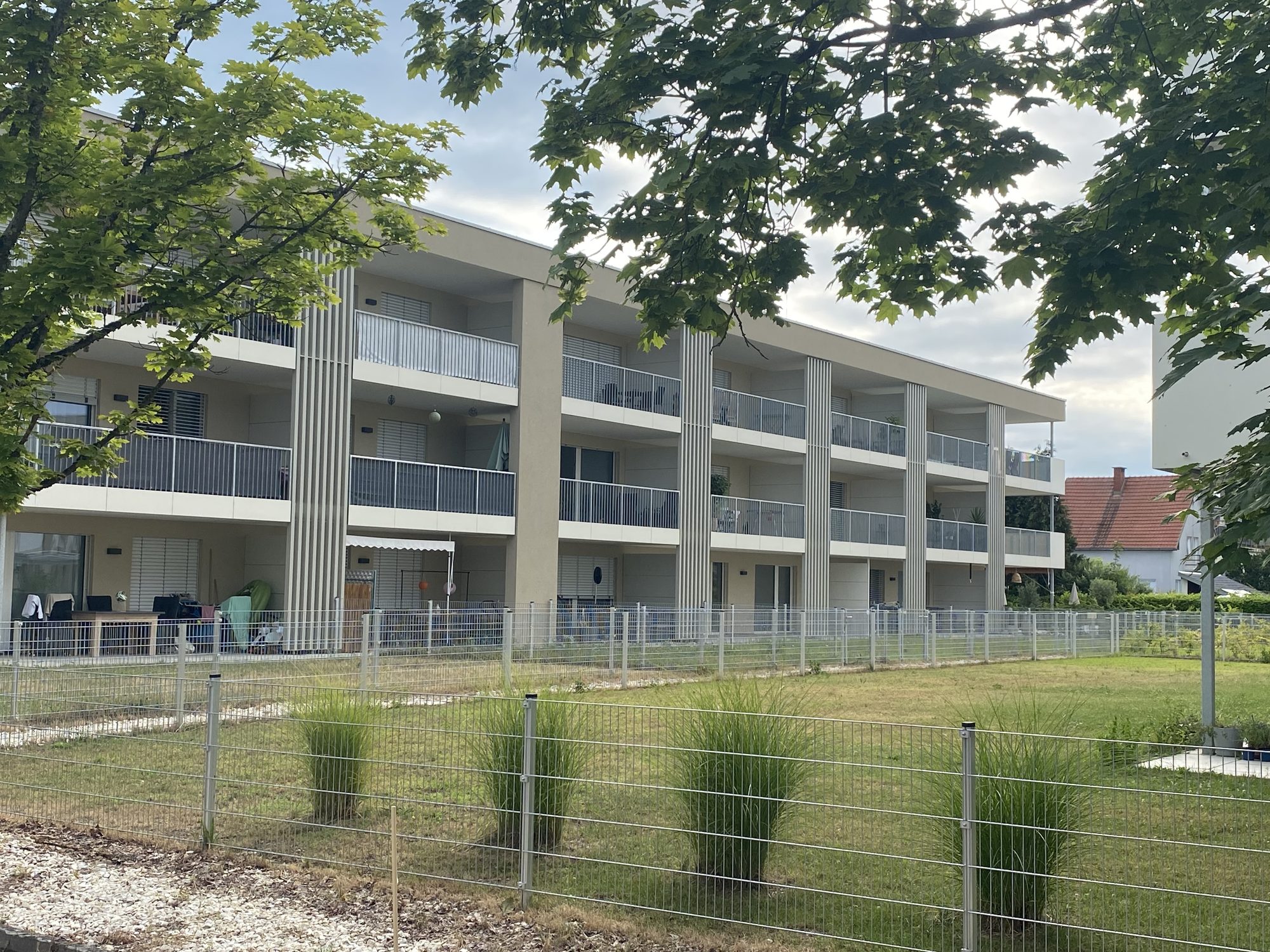 Das fertiggestellte Wohnprojekt LICHT:blick in Klagenfurt: dreigeschossiger Baukörper mit Balkonen, davor Rasen und Zaun