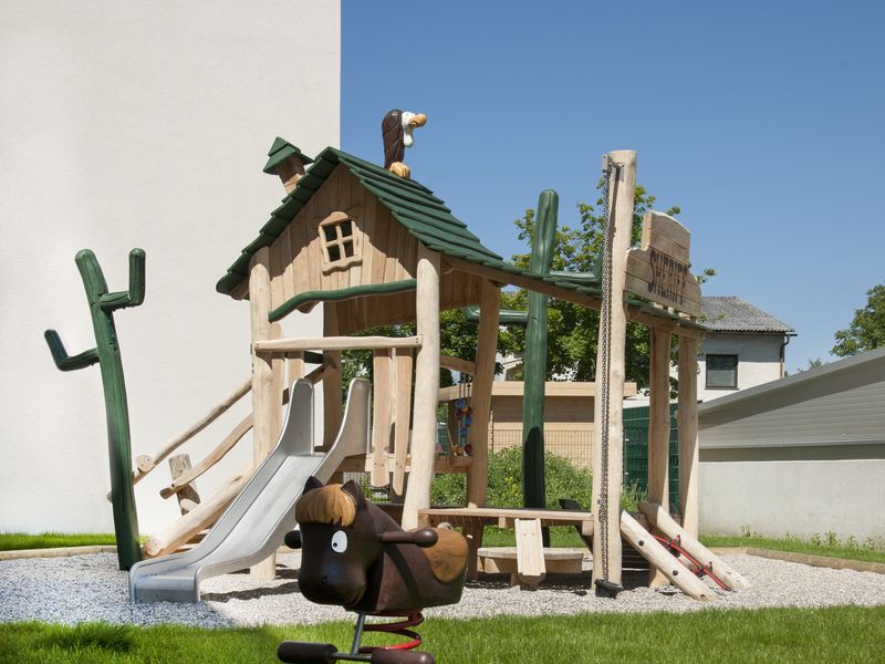 Spielplatz mit Holz-Spielhaus vor einem Wohnhaus