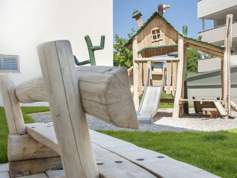Holzwippe auf dem Spielplatz, dahinter Balkone